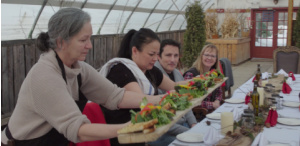 Visitors gather around a dining table at Prairie Gardens and are served locally grown culinary dishes.